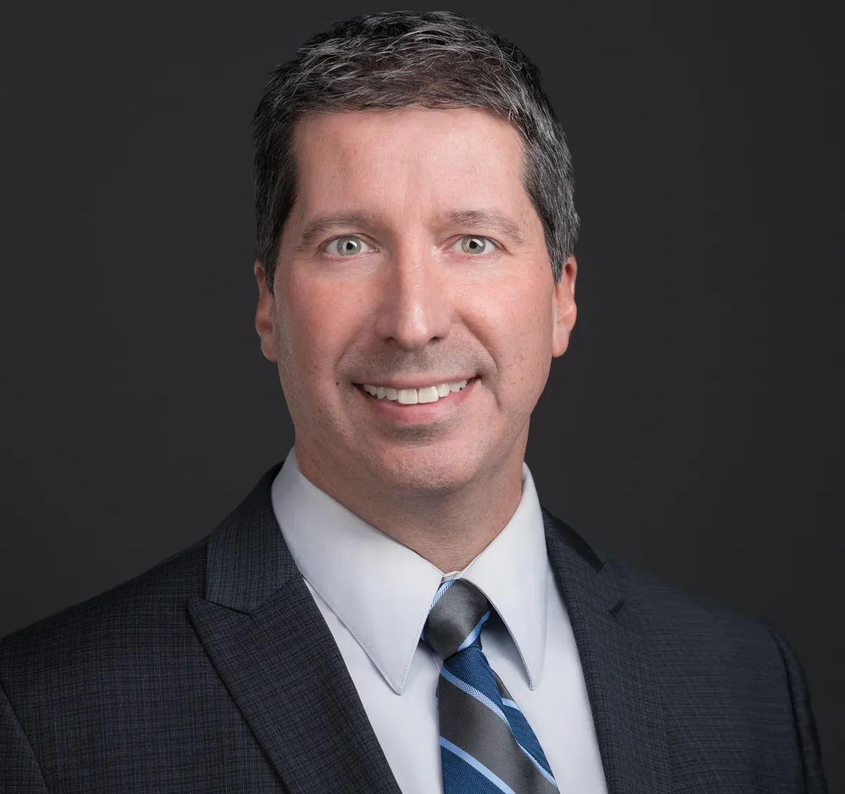 Professional headshot of a man in a suit and tie with a neutral background.